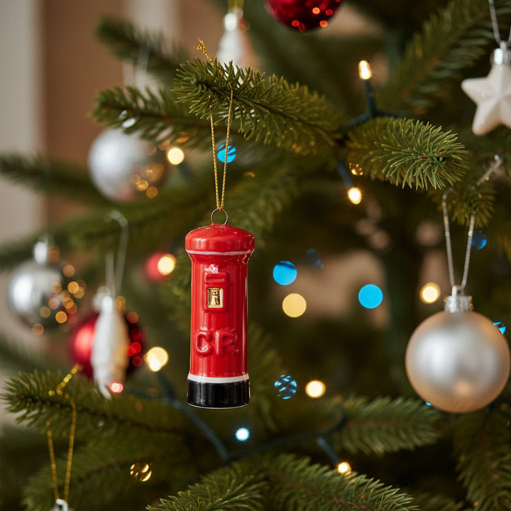 A red post box Christmas ornament with a gold hanging string, featuring a gold front detail and a black base, shown against a plain white background.