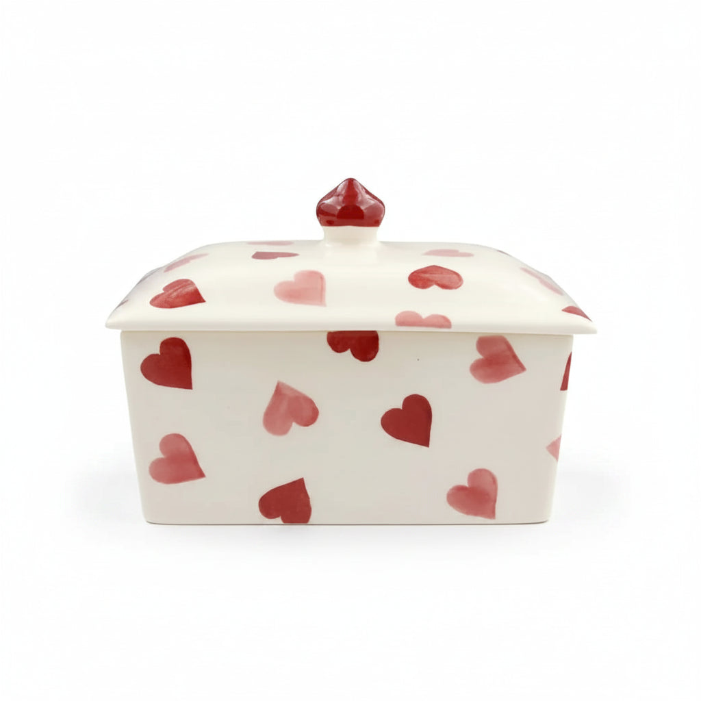 White ceramic butter dish with red heart patterns on a white background