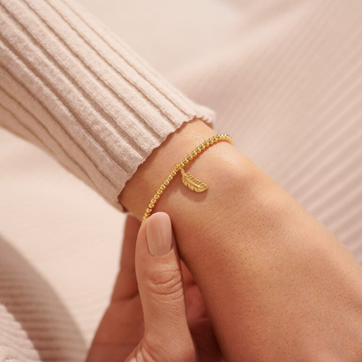 Gold "A Little Feathers Appear" bracelet by Joma Jewellery featuring delicate feather charms on a gold chain.