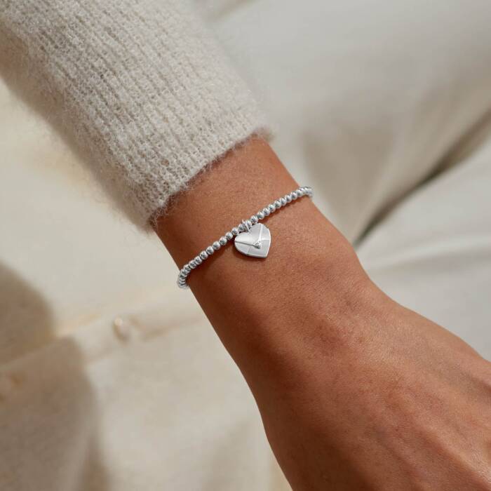Joma Jewellery Little Sending Love Bracelet with heart charm, delicate gold-tone chain, and engraved message, on a neutral background.