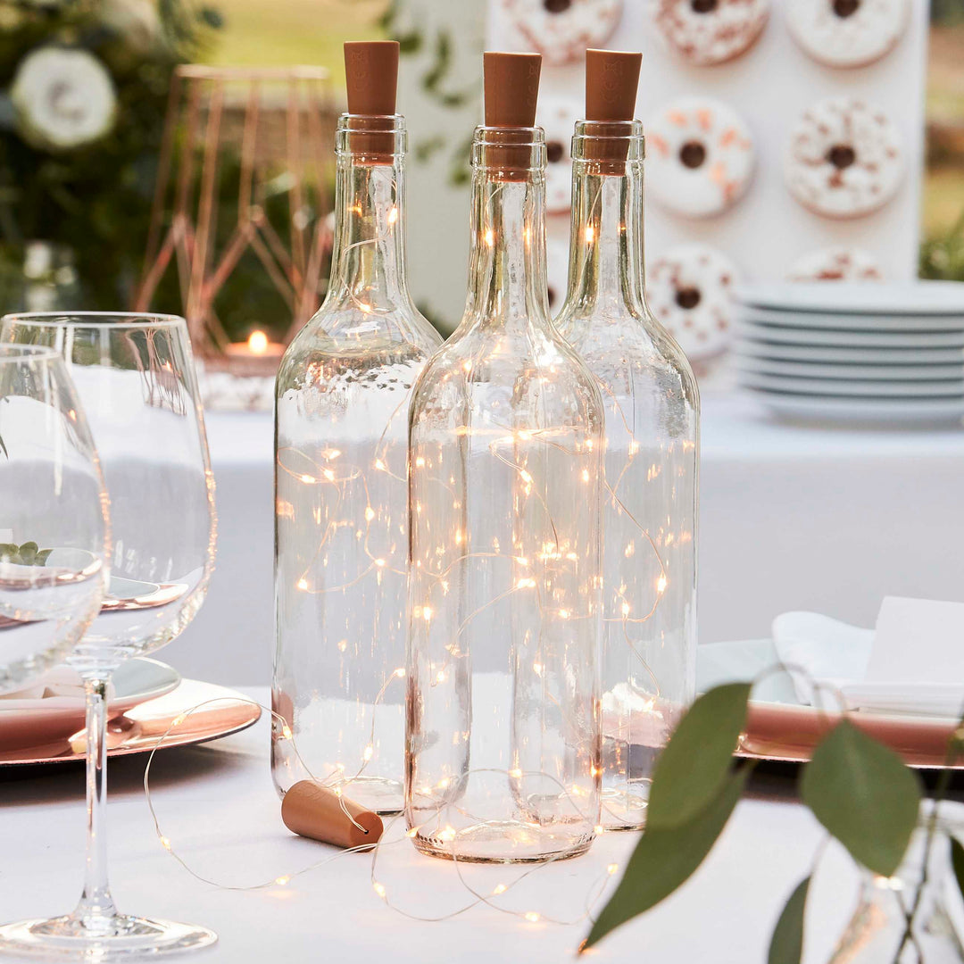 Cork bottle lights with botanical design by Ginger Ray, ideal for wedding decor, featuring glowing string lights inside cork bottles.