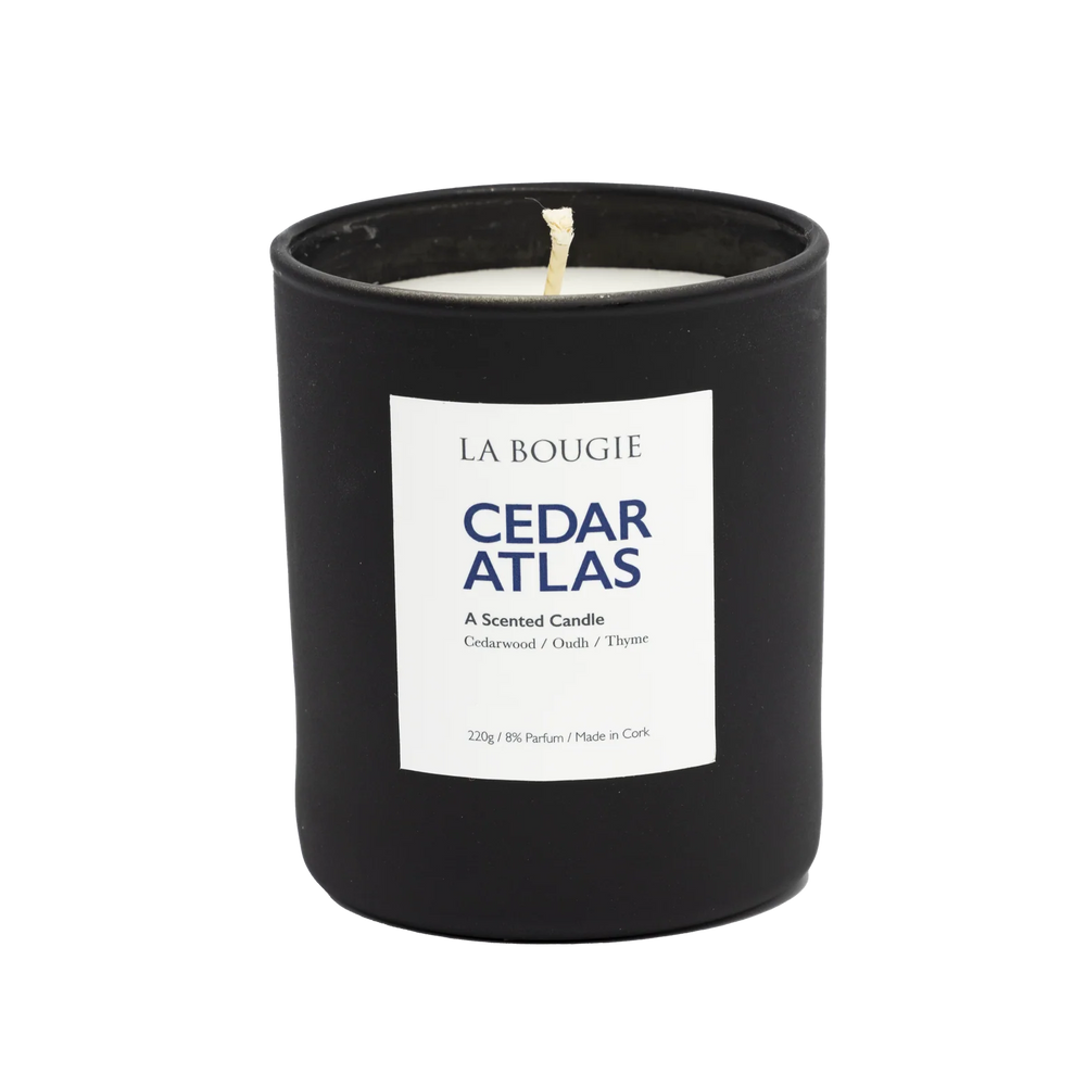 Cedar Atlas Candle by Cornucopia Home and Gift, La Bougie brand, with a tall glass container and a lit cedar-scented candle inside.