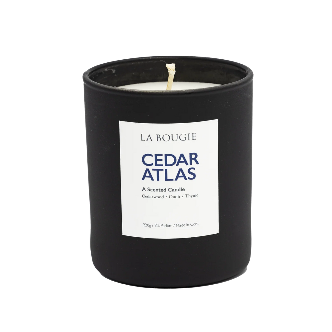 Cedar Atlas Candle by Cornucopia Home and Gift, La Bougie brand, with a tall glass container and a lit cedar-scented candle inside.