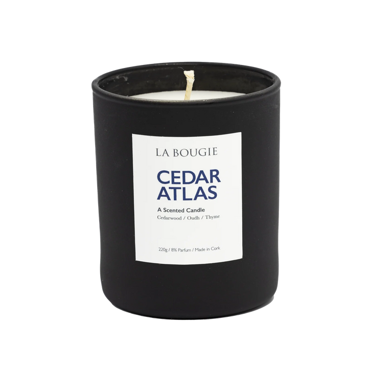 Cedar Atlas Candle by Cornucopia Home and Gift, La Bougie brand, with a tall glass container and a lit cedar-scented candle inside.