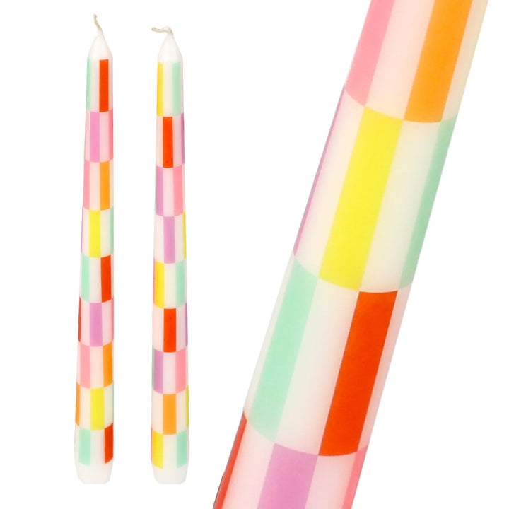 Two multi-colored check taper dinner candles from Cornucopia Home and Gift by Talking Tables, arranged on a dinner table.
