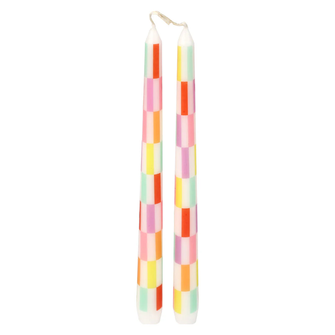 Two multi-colored check taper dinner candles by Cornucopia Home and Gift from Talking Tables, arranged on a dining table.