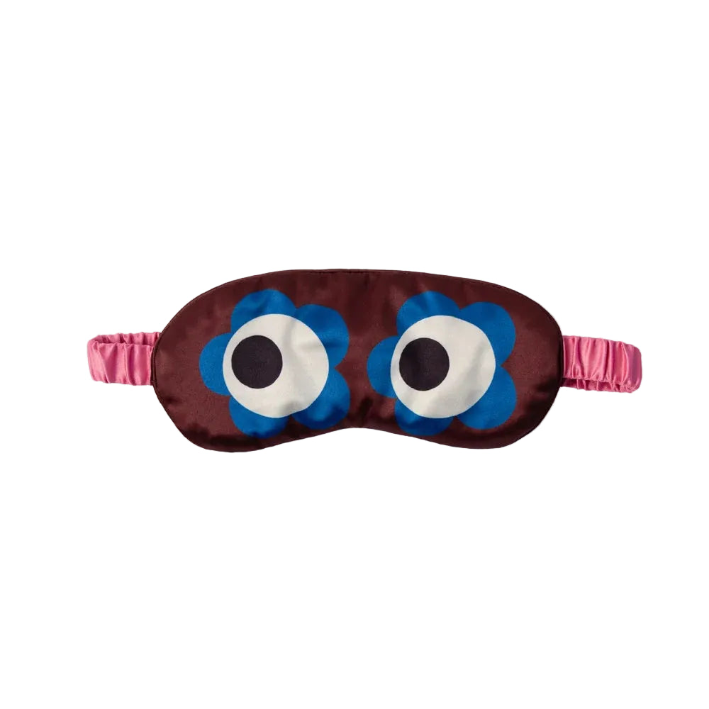 A novelty sleep mask featuring a dark brown satin body with two large cartoon eyes made of blue flower petals, white circles, and black centers, finished with a pink elastic strap.