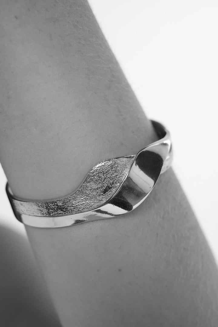 Silver Wave bangle by Tutti &amp; Co featuring a sleek, wavy design, displayed on a neutral background.