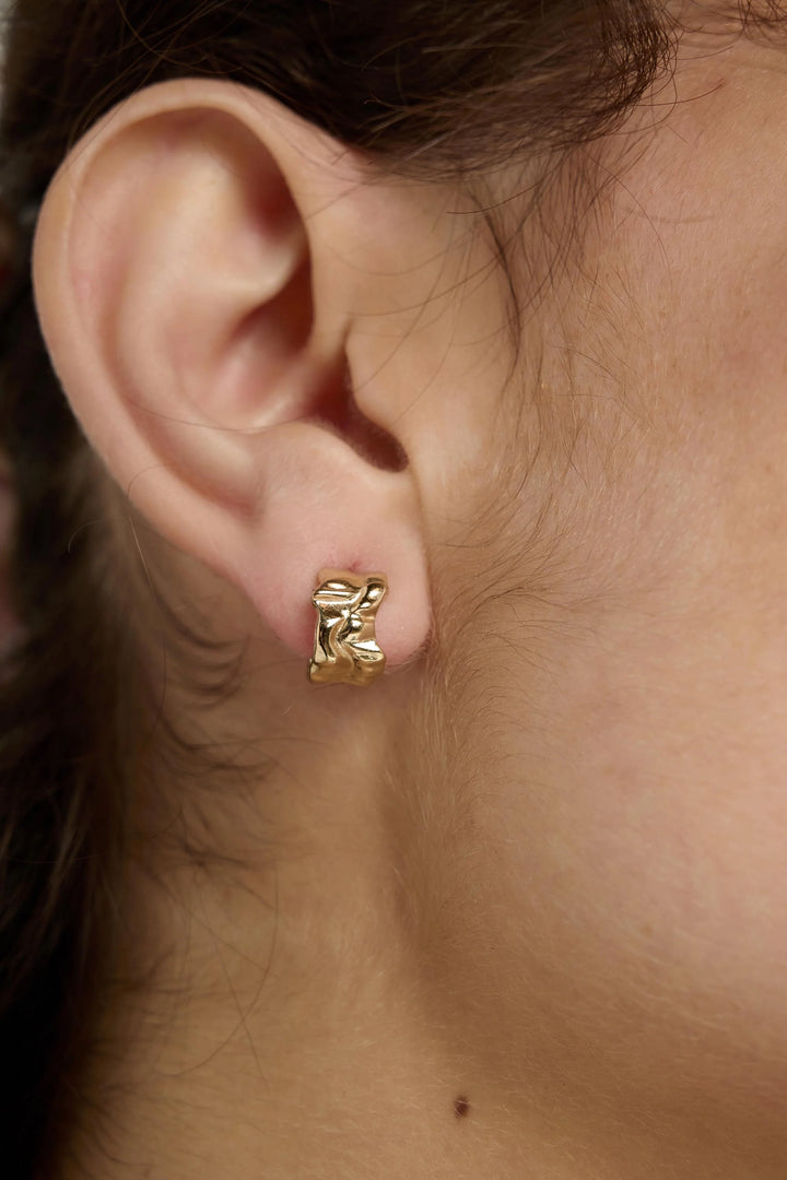 Gold Ripple Earrings by Tutti &amp; Co featuring a wavy, textured design, displayed on a neutral background.