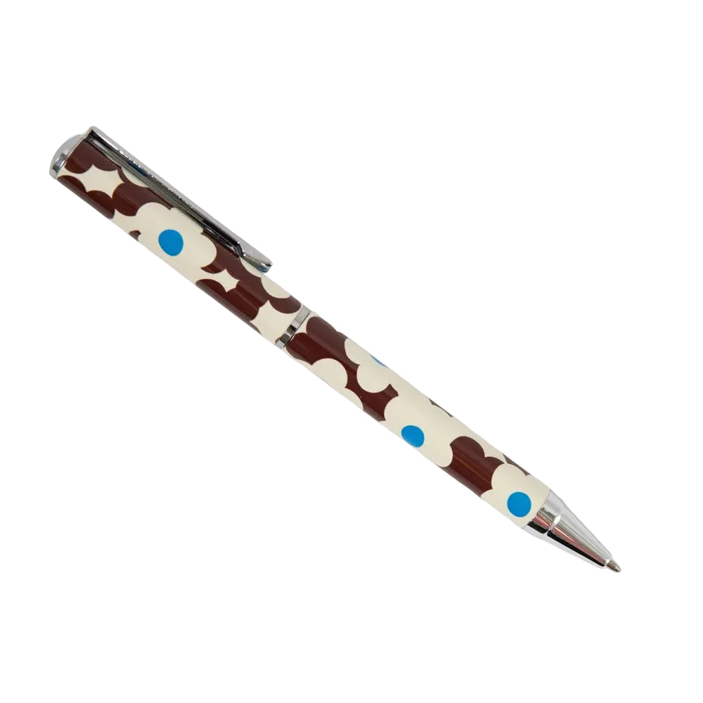 A ballpoint pen with a brown and cream cow print pattern, accented with small blue dots, shown on a plain light gray background.