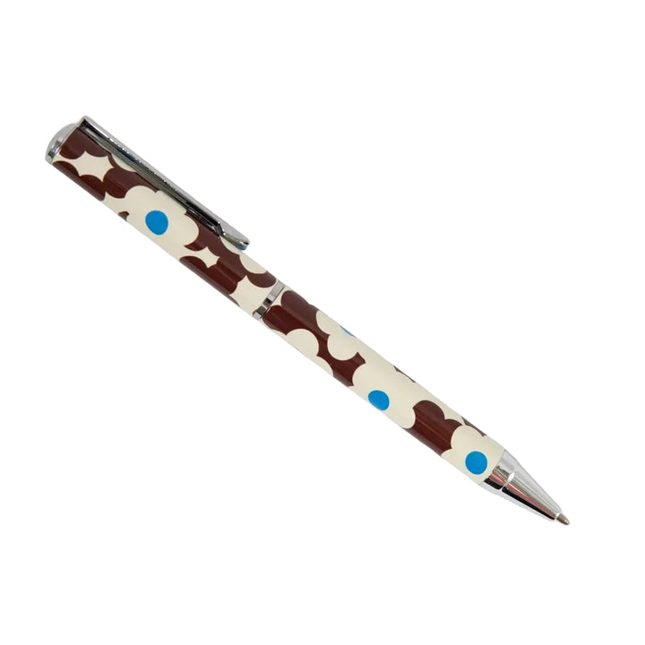 A ballpoint pen with a brown and cream cow print pattern, accented with small blue dots, shown on a plain light gray background.