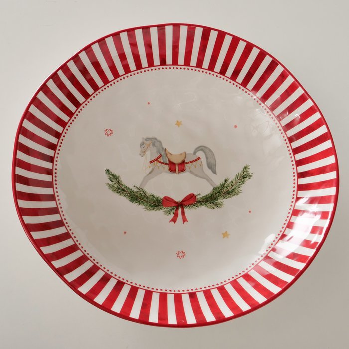 A round ceramic plate with a festive holiday design, featuring a red and white striped rim, a central illustration of a rocking horse under a green wreath with a red bow, and small gold stars on a white background.