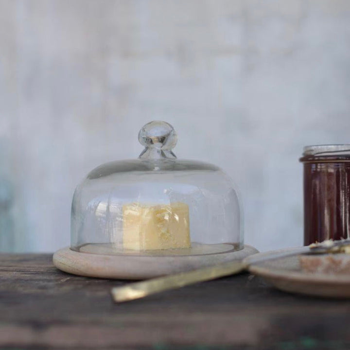 Clear recycled glass cake dome by Nkuku, featuring a round shape and smooth glass surface for showcasing baked goods.