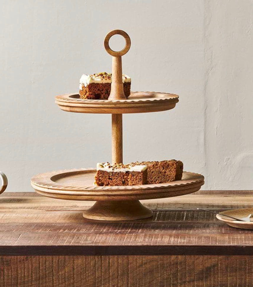 Nkuku Gavivi mango wood cake stand with a natural finish, featuring a round flat surface and sturdy base for serving desserts.