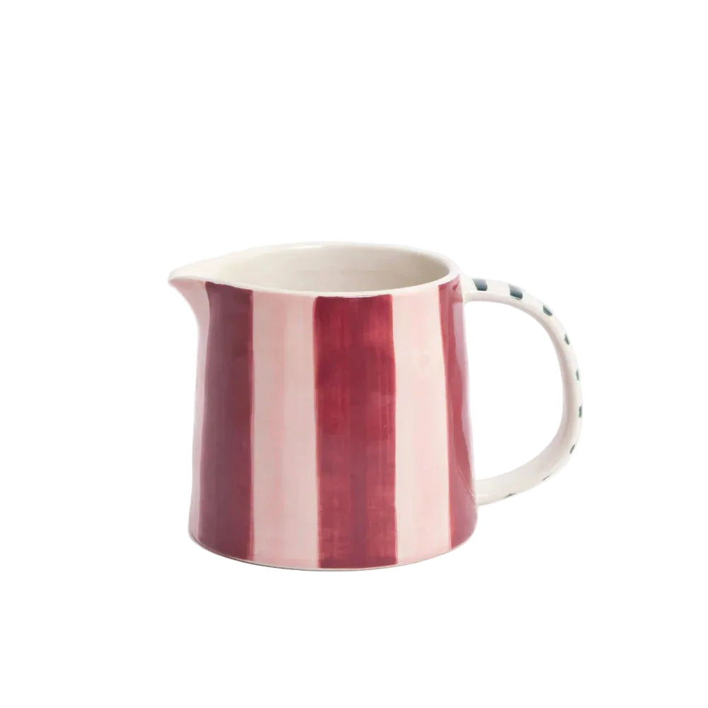 A ceramic pitcher with vertical stripes in deep red and light pink on the exterior, with a white handle and a dotted pattern on the side, set against a plain light gray background.