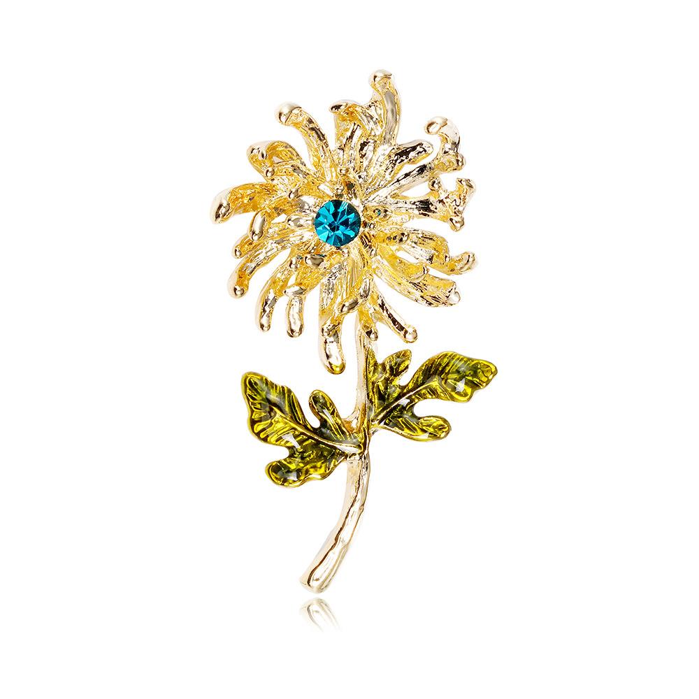 White leaf-shaped brooch featuring a gold dandelion design from Cornucopia Home and Gift.