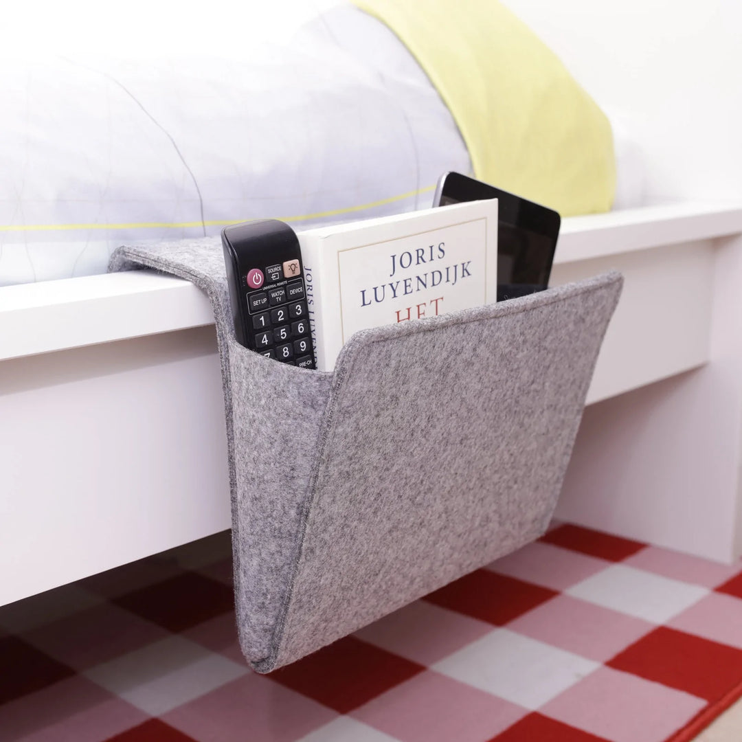 Kikkerland bedside pocket organizer hanging on a bed frame, made of fabric with multiple pockets for bedside essentials.